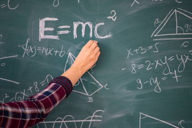 Tebeşiri tutan ve tahtaya matematiksel denklemler yazan bir elin yakın plan çekimi. Eğitim kavramı.