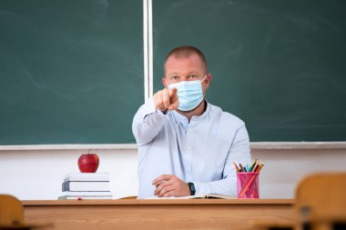  Sınıfta maskeli bir öğretmen var. Coronavirus salgını sırasında sosyal uzaklık ve sınıf güvenliği