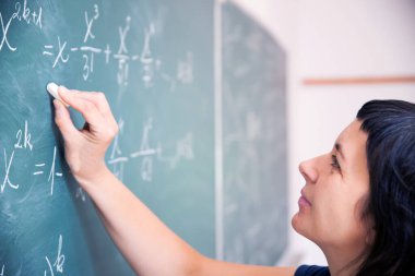 Okulda matematik dersi sırasında tahtaya yazı yazan öğretmen ya da öğrenci..