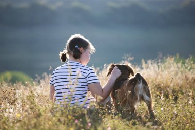 Köpeğiyle yaz otlağında oturan bir çocuk.