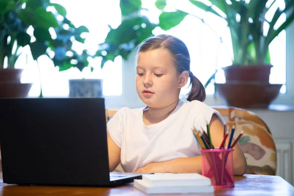 Distance learning, online education. School girl watching online education classes and doing school homework. COVID-19 pandemic forces children online learning.