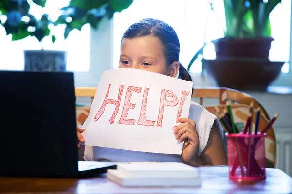 Distance learning concept. School girl holding help text during online education classes. COVID-19 pandemic forces children online learning.