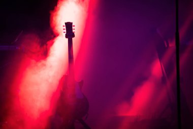 Sahnede, ışık demeti altında, fotokopi çekilen dumanlı akustik gitar. Müzik, yaz festivali konsepti.