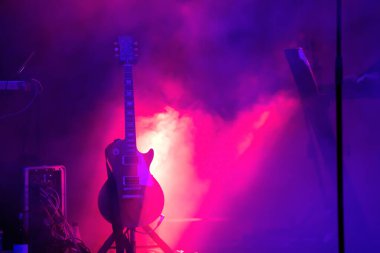 Sahnede, ışık demeti altında, fotokopi çekilen dumanlı akustik gitar. Müzik, yaz festivali konsepti.