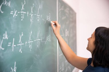 Okulda matematik dersi sırasında tahtaya yazı yazan öğretmen ya da öğrenci..