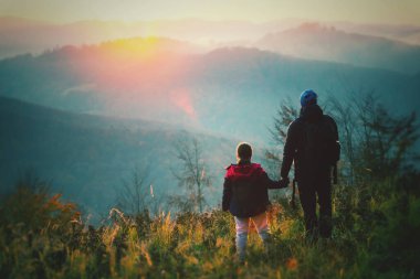 Baba ve kızı gün batımında güzel bir sonbahar ormanında güneşin ve manzaranın tadını çıkarıyorlar. Mutlu aile kavramı.