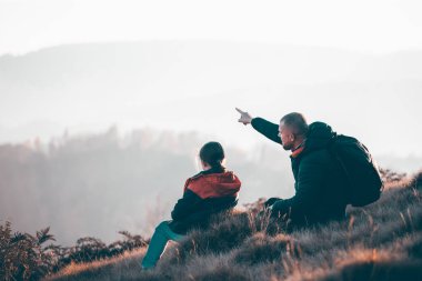 Baba ve kızı gün batımında güzel bir sonbahar ormanında güneşin ve manzaranın tadını çıkarıyorlar. Mutlu aile kavramı.