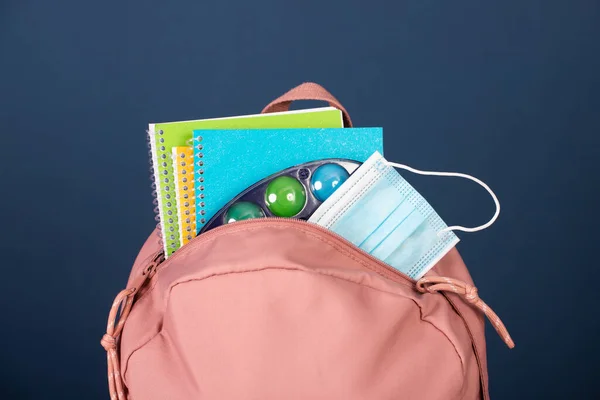 Backpack with school supplies and medical mask. COVID-19 prevention while going back to school and new normal concept.