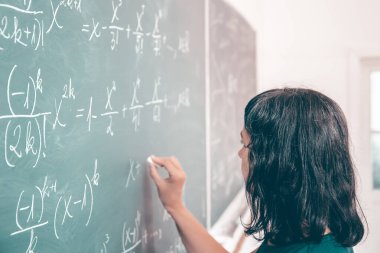 Okulda matematik dersi sırasında tahtaya yazı yazan öğretmen ya da öğrenci..