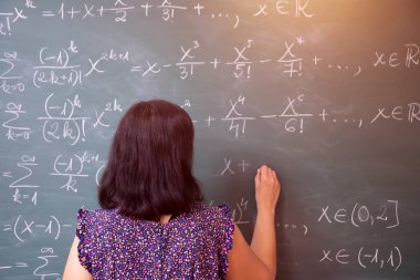 Okulda matematik dersi sırasında tahtaya yazı yazan öğretmen ya da öğrenci..
