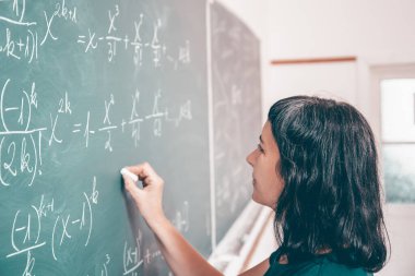Okulda matematik dersi sırasında tahtaya yazı yazan öğretmen ya da öğrenci..