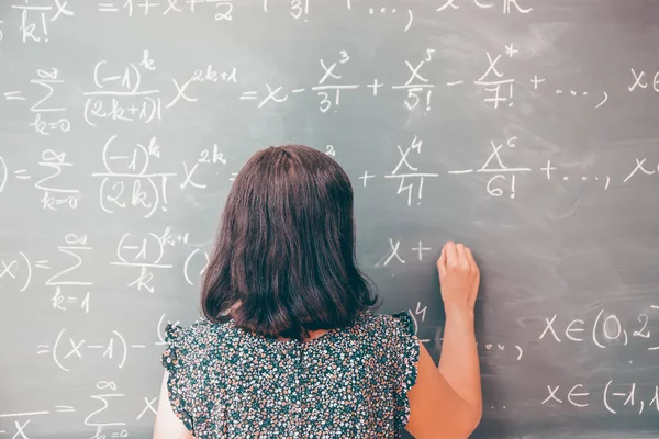 Teacher or student writing on blackboard during math lesson in school classroom.