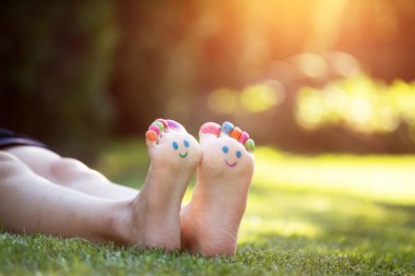 Yeşil çimenlerde gülümseyen renkli yüzle boyanmış çocuk ayakları.