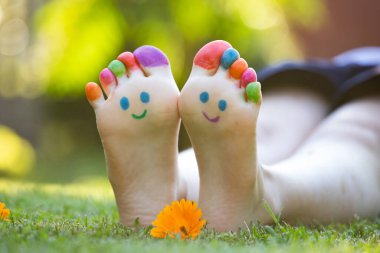 Yeşil çimenlerde gülümseyen renkli yüzle boyanmış çocuk ayakları.