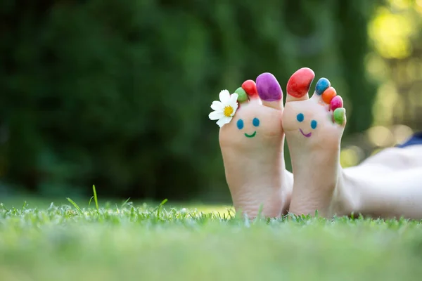 孩子的脚在绿草上画着五彩缤纷的笑脸 — 图库照片