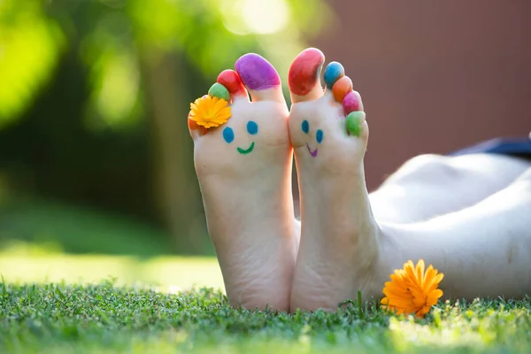 緑の草の中にカラフルな笑顔で描かれた子供の足 — ストック写真