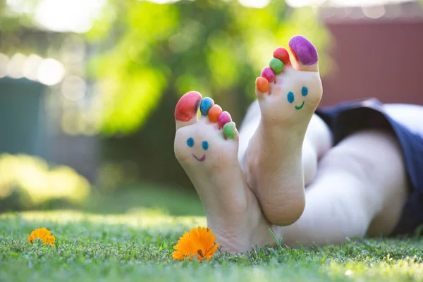 Child feet painted with colorful smiling face in green grass