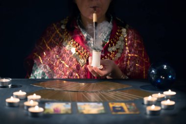 Falcı elinde mumların yanındaki masada tarot kartlarıyla. Tarot kartları kristal kürenin üzerine yayılmış. Tahmin konsepti..
