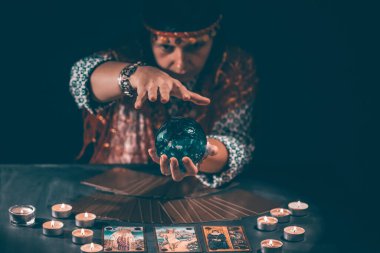 Falcı elinde mumların yanındaki masada tarot kartlarıyla. Tarot kartları kristal kürenin üzerine yayılmış. Tahmin konsepti..