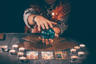 Falcı elinde mumların yanındaki masada tarot kartlarıyla. Tarot kartları kristal kürenin üzerine yayılmış. Tahmin konsepti..