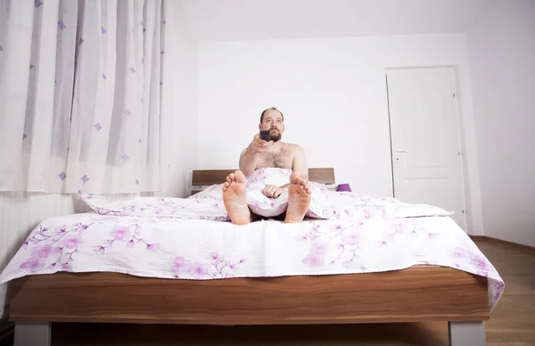 Man watching TV from the bed with remote-control — Stock Photo, Image