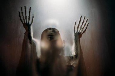 Creepy skeleton figure with skull behind matte glass. Halloween festival concept.Blurred picture