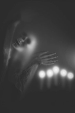 Creepy skeleton figure with skull and candle lights behind matte glass. Halloween festival concept.Blurred picture