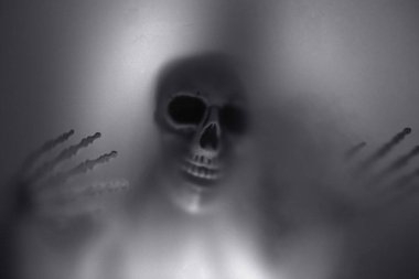 Creepy skeleton figure with skull and candle lights behind matte glass. Halloween festival concept.Blurred picture