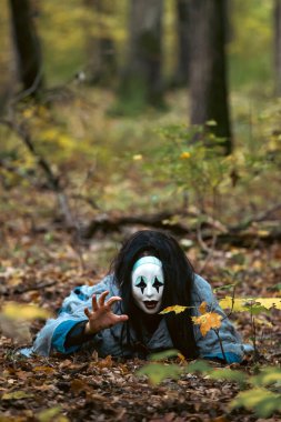 Cadılar Bayramı konsepti: Korkunç maskeli ve sonbahar ormanlarında sürünen tuhaf elbiseli hayalet kadın..