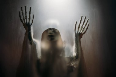 Creepy skeleton figure with skull behind matte glass. Halloween festival concept.Blurred picture