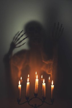 Creepy skeleton figure with skull and candlelights behind matte glass. Halloween festival concept.Blurred picture