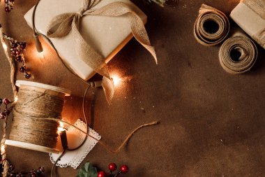 Kahverengi arka planda hediyeler, mücevherler, makaslar ve süslemelerle yaratıcı Noel el sanatları sahnesi. DIY tatil projeleri, festival temaları ve sezonluk tasarım için mükemmel.