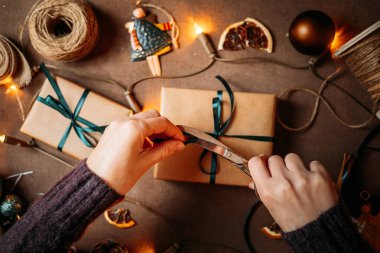 Kadınların Noel hediyesi kutusunu süslediği en üst manzara, parıldayan tatil ışıkları ve sıcak atmosferdeki şenlikli dekorasyonlar, Noel arifesi hazırlıkları.