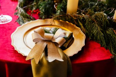 Altın tabağa yakın çekim ve güzel düzenlenmiş kırmızı ve Cooper aksanlı Noel yemeği masası..