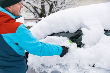 Kışın yoğun kar yağışı sonrasında arabadaki karı temizleyen adam