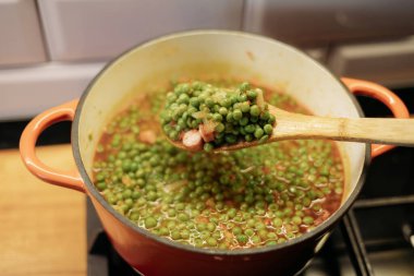 Kırmızı bir tencerede yeşil bezelye çömleği pişirmek. Macar yemeği.