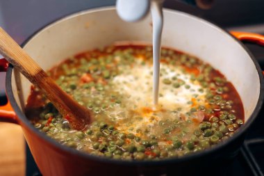 Kırmızı bir tencerede yeşil bezelye çömleği pişirmek. Macar yemeği.