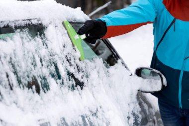İnsanlar kış sabahı evlerinin önünde arabalarından kar çıkarırlar.