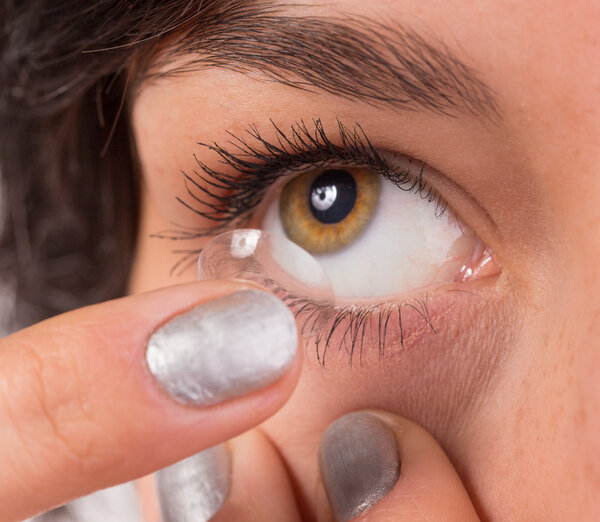 Young woman putting contact lens in her eye.