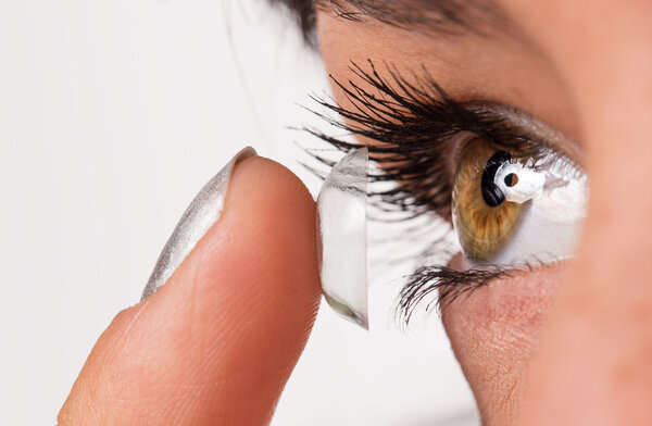 Young woman putting contact lens in her eye.