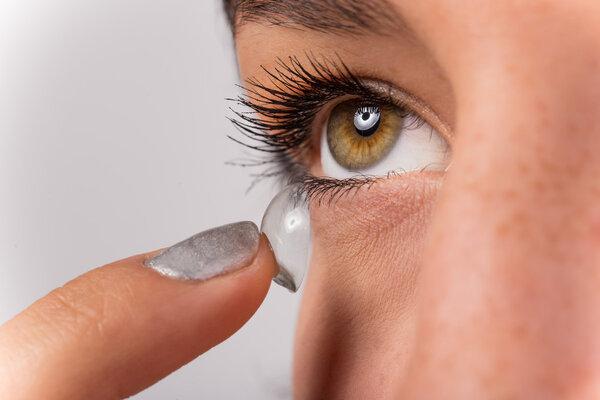 Young woman putting contact lens in her eye.