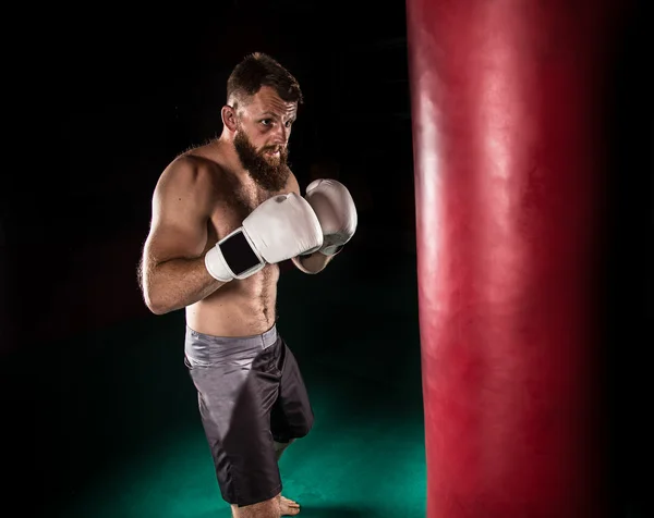 Svalnatý bokovky bojovník dává silný kop během praxe s boxovací pytel. — Stock fotografie