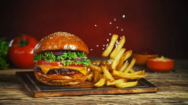 Frites tombent à côté de cheeseburger, couché sur la planche à découper en bois vintage. — Photo