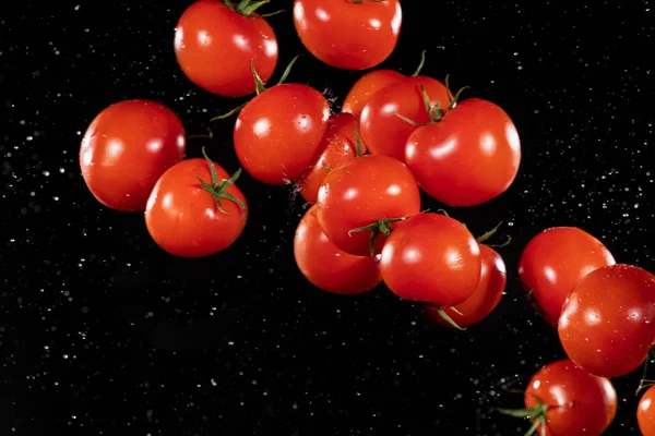 Fliegende Kirschtomaten, isoliert auf schwarzem Hintergrund. — Stockfoto