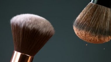 Makyaj fırçaları koyu arkaplan ve küçük kozmetik parçacıkları üzerinde birbirlerine dokunurlar.