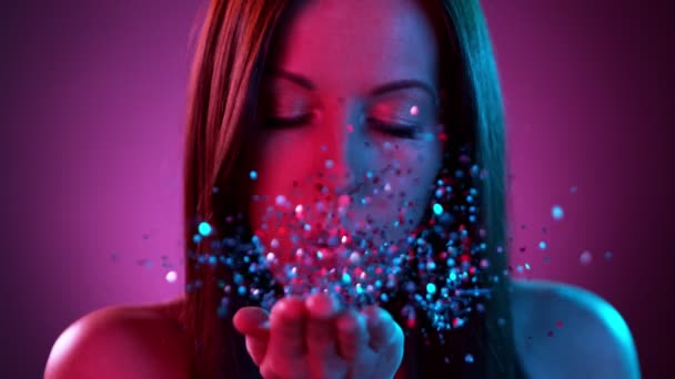 Sexy brunette woman with blowing neon glitters towards the camera. — Stock Video