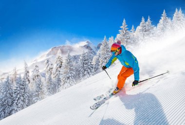 Güneşli bir günde yokuş aşağı kayak yapan kayakçı.