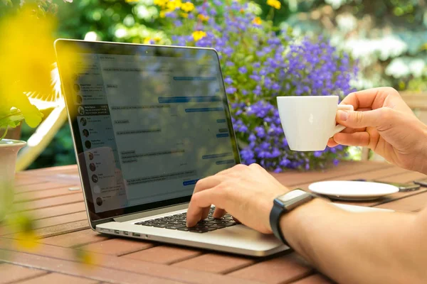 Mann arbeitet am Laptop im Garten und trinkt Kaffee. — Stockfoto