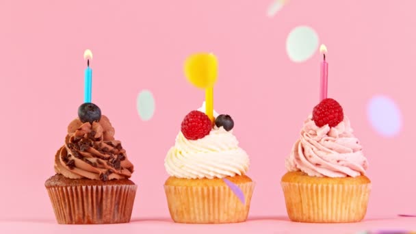 Gâteaux de tasse d'anniversaire avec des bougies colorées brûlantes sur fond bleu pastel. — Video