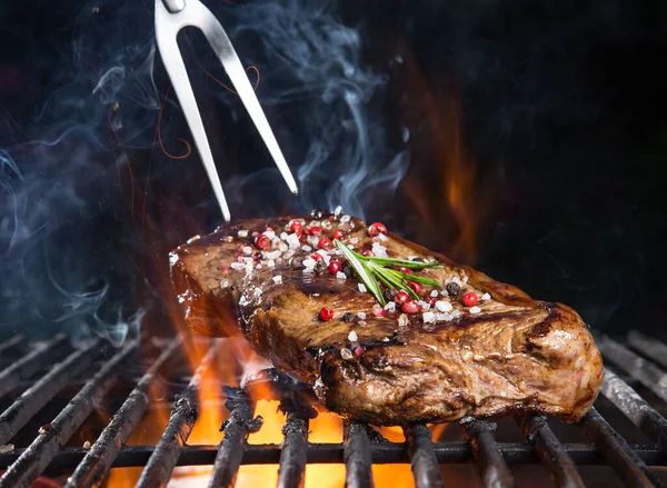 Bife saboroso na grelha de ferro fundido com chamas de fogo. — Fotografia de Stock